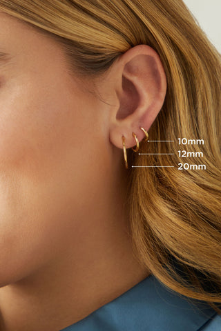 Image shows model in profile wearing three different 14 karat gold huggie hoop earrings ranging in size from 10mm to 20mm.