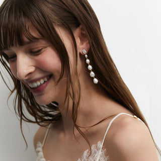 Model smiling with eyes closed wearing a wedding gown and Nadri pearl linear earrings.