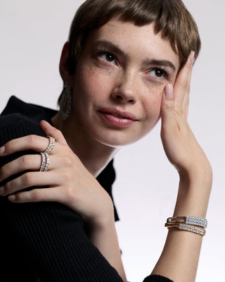 A MODEL WITH SHORT RED HAIR LEANING ON HER PALM AS SHE LOOKS UPWARD AND HER OPPOSITE HAND CUPS HER SHOULDER, ALL WHILE SHE WEARS JEWELRY FROM NADRI’S TWINNIE COLLECTION