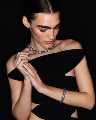 A MODEL LOOKING DOWN WITH HER ARMS CASUALLY ACROSS HER, WEARING A BLACK DRESS AND JEWELRY FROM NADRI’S TURN UP THE VOLUME COLLECTION