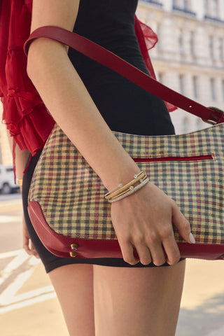 CLOSE UP OF A MODEL’S HAND AT HER SIDE HOLDING A GINGHAM PRINT BAG, AS SHE WEARS A STACK OF HALF PAVE CZ HINGED OVAL BANGLES
