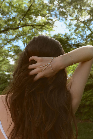 THE BACK OF A MODEL’S HEAD AS SHE RUNS HER HAND THROUGH HER LONG BRUNETTE HAIR AND WEARS THE EVERLEIGH HAND CHAIN BRACELET