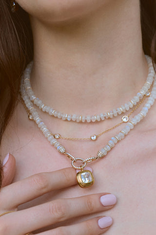 CLOSE UP OF A MODEL’S NECK WEARING A NECKLACE STACK WITH THE BOUJEE BEADS MOONSTONE LONG NECKLACE, AS HER HAND IS LIFTED UP TOUCHING THE NECKLACE PENDANT. 