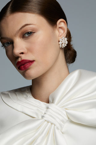 MODEL WEARING LONDON LARGE CLUSTER PEARL EARRINGS. HER HAIR IS IN A SLICK BUN WITH RED LIPSTICK ON. WEARING A WHITE BRIDAL BOW TOP. 