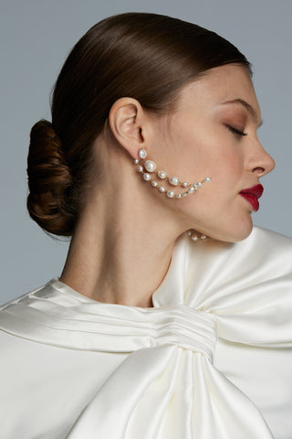 MODEL WEARING LONDON LONG LINEAR FRONTBACK PEARL EARRINGS. HER EYES ARE CLOSED AND HER HEAD IS TURNED AS THE EARRINGS CONTINUE TO SWING GENTLY FROM HER EARS.