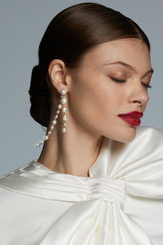 MODEL WEARING LONDON LONG LINEAR FRONTBACK PEARL EARRINGS. HER EYES ARE CLOSED AS THE EARRINGS SWING GENTLY FROM HER EARS.