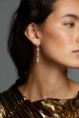 LUXOR KITE CZ LINEAR EARRINGS ON MODEL. IT IS A CLOSE UP IMAGE WITH THE MODEL FACING SIDEWAYS AND HAIR TUCKED BEHIND HER EARRINGS. 