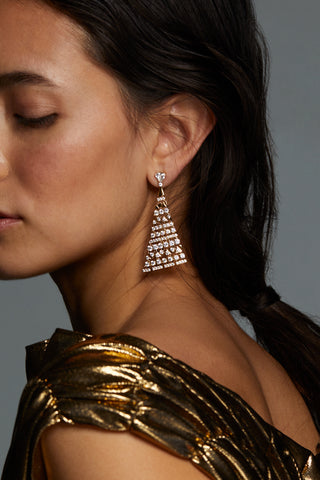 LUXOR TRIANGLE CZ DROP EARRINGS ON MODEL. SHE IS TURNING SIDEWAYS WITH EYES CLOSED WEARING A GOLD METALLIC DRESS. ONE OF THE EARRINGS IS CLEARLY VISIBLE IN FOCUS SHOWING DETAILED PATTERN. 