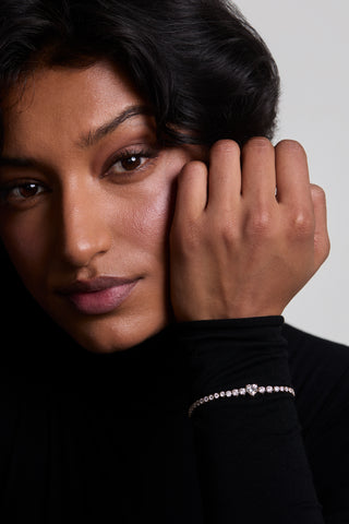 CLOSE UP OF MODEL IN A BLACK TOP HOLDING HER HAND UP TO HER FACE, WEARING THE ASTRID HEART TENNIS BRACELET