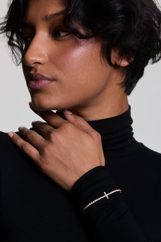 A MODEL WEARING A BLACK TURTLENECK WITH HER HAND PLACED ACROSS HER CHEST, WEARING THE ASTRID CROSS TENNIS BRACELET