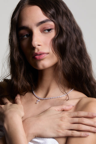 CLOSE UP OF A MODEL LOOKING TO THE SIDE WITH HER HANDS CROSSED ON HER CHEST, WEARING THE ASTRID CROSS TENNIS NECKLACE