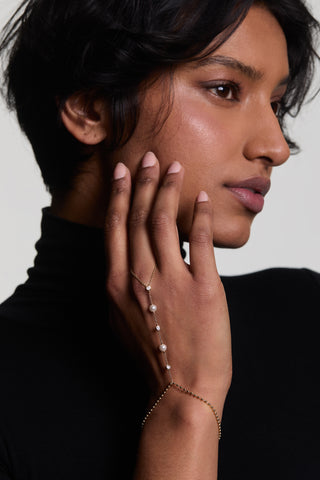 A MODEL TURNING TO THE SIDE WITH HER HAND PLACED ON HER CHEEK, WEARING THE ESME PEARL HAND CHAIN BRACELET AND A BLACK TURTLENECK TOP