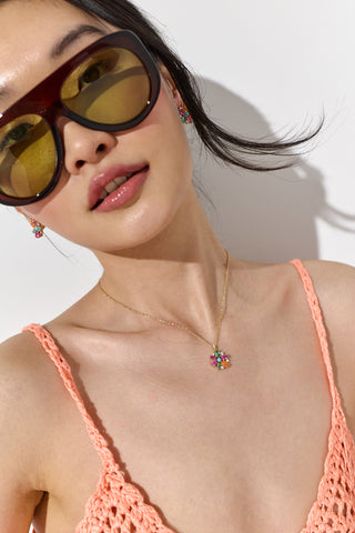 CLOSE UP OF A MODEL LOOKING AT THE CAMERA WEARING AN ORANGE TOP, THE FRIEDA FLORAL PENDANT NECKLACE, AND SUNGLASSES