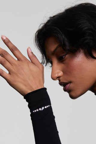 CLOSE UP OF A MODEL’S SIDE PROFILE AS SHE RAISES HER HAND UP TO HER FACE, WEARING A BLACK SHIRT WITH THE LUCIA ADJUSTABLE LINE BRACELET STACKED OVER THE SLEEVE