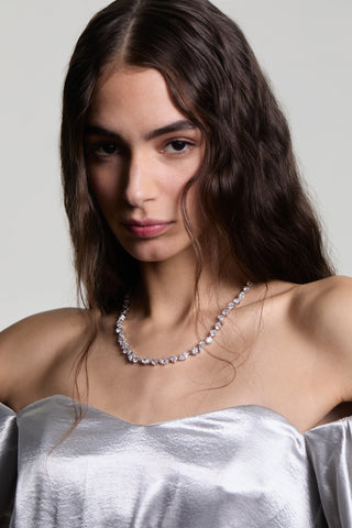 A MODEL LOOKING AT THE CAMERA WITH HER HAIR FALLING IN FRONT OF HER FACE AS SHE WEARS THE LUCIA MIXED CZ NECKLACE WITH A WHITE TOP