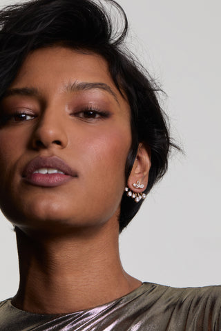 A CLOSE-UP OF A MODEL LOOKING AT THE CAMERA WEARING LUCIA FRONTBACK JACKET EARRINGS, STYLED WITH SHORT HAIR AND A METALLIC TOP