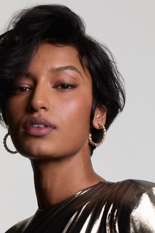 CLOSE UP OF A MODEL LOOKING AT THE CAMERA, WEARING LUCIA PATTERN C HOOP EARRINGS AND A METALLIC TOP, WITH HER SHORT HAIR FRAMING HER FACE