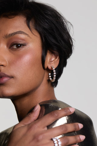 CLOSE UP OF HALF OF A MODEL’S FACE LOOKING AT THE CAMERA AS HER HAND RESTS ON HER SHOULDER WEARING LUCIA PATTERN C HOOP EARRINGS