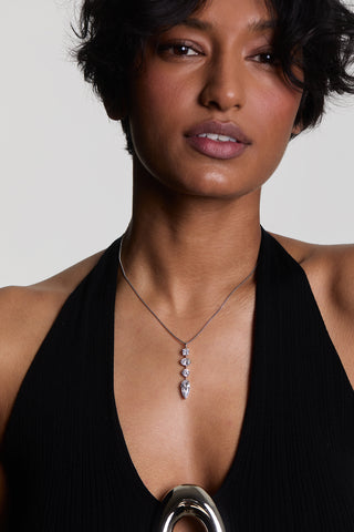 A MODEL LOOKING AT THE CAMERA WEARING THE LUCIA LINEAR PENDANT NECKLACE, STYLED WITH A BLACK HALTER TOP