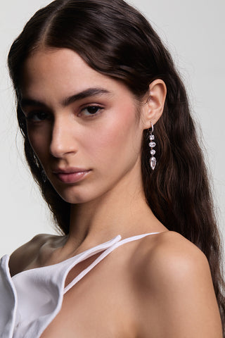 A MODEL LOOKING AT THE CAMERA WITH HER HAIR TUCKED BEHIND HER EAR WEARING LUCIA LINEAR LEVERBACK EARRINGS AND A WHITE, STRAPPY TOP