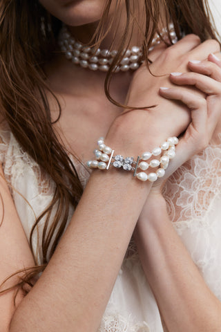 MODEL WEARING MADRID 3 ROW FRESHWATER PEARL BRACELET. IT IS A CLOSE UP IMAGE OF HER WRIST WITH HER HAND UP TO HER CHEST. 