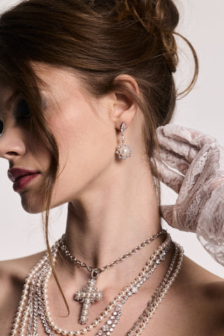 SIDE PROFILE OF A MODEL LOOKING AWAY WITH HER HAND ON HER NECK, WEARING THE MATERIAL PEARL FRAMED DROP EARRINGS AND CHUNKY NECKLACES.