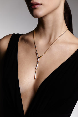 CLOSE UP OF MODEL WEARING PHENOM FRONTAL Y NECKLACE WITH A DEEP V-NECK BLACK DRESS. 