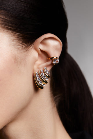 Close up of a model's ear wearing the Phenom Single Emerald Cuff earrings in gold and the Phenom Multi-J Hoop earrings in gold. 