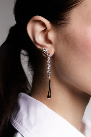 PHENOM LONG LINEAR EARRINGS ON MODEL. HER HAIR IS IN A LOW PONYTAIL WEARING A WHITE COLARED SHIRT. 