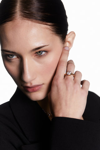 MODEL WEARING PHENOM EMERALD RING.  ITS A CLOSE UP IMAGE OF HER FACE WITH HER HAND UP TO HER EAR. HER HAIR IS IN A PONYTAIL AND SHES WEARING A BLACK LONG SLEEVE COLARED SHIRT. 