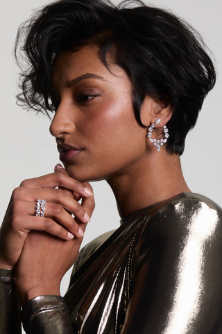 SIDE PROFILE OF A MODEL LOOKING AWAY WITH HER HANDS RESTING BELOW HER CHIN, WEARING THE RIVIERA FRONTBACK EARRINGS AND A METALLIC TOP