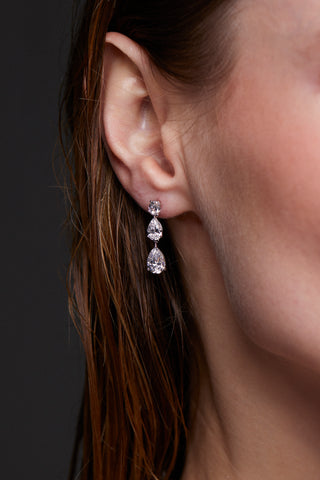 Close-up of a model wearing CHLOE PEAR DROP EARRINGS in RHODIUM PLATING against a dark background