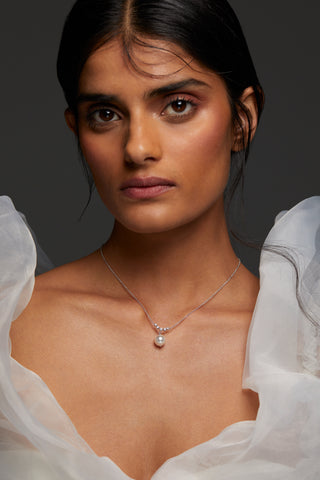 MODEL WEARING VENUS PEARL DROP NECKLACE. SHE IS LOOKING DIRECTLY INTO THE CAMERA WITH HER HAIR BACK IN A LOW BUN WEARING PUFFY WHITE SLEEVE DRESS. 