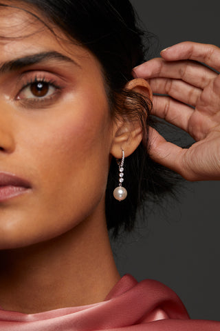 CLOSE UP IMAGE OF MODEL WEARING VENUS PEARL DROP LEVERBACK EARRINGS. HALF HER FACE IS IN FRAME WITH HER HAND UP TO HER EAR. SHE HAS ON A HIGH NECK CHIFFON PINK TOP. 