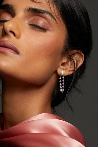 MODEL WEARING VENUS PEARL FRONTBACK EARRINGS. IT IS A CLOSE UP IMAGE WITH HER HAIR IN A LOW BUN AND EYES CLOSED. 