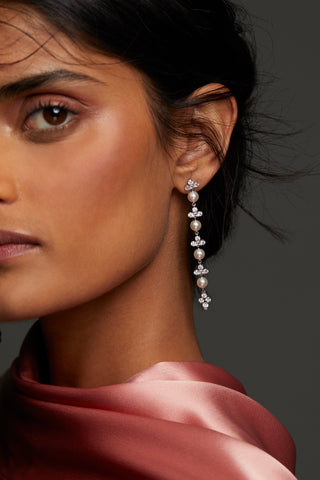 CLOSE UP IMAGE OF MODEL WEARING VENUS PEARL LONG LINEAR EARRINGS. HER HAIR IS IN A LOW BUN WITH A PINK CHIFFON HIGH NECK TOP. 