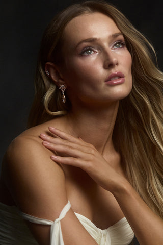 A MODEL LOOKING UPWARD WITH HER HAND RAISED TO HER SHOULDER, AS SHE WEARS THE CANNES DROP EARRINGS