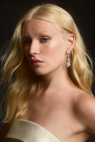 A MODEL SLIGHTLY TURNED TO THE SIDE WITH HER BLONDE HAIR BLOWING NEXT TO HER, AS SHE WEARS THE CANNES HOOP DROP EARRINGS