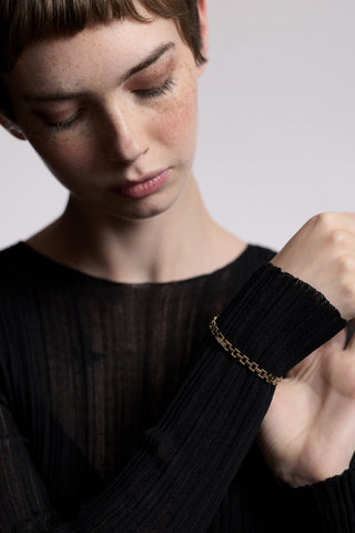 A MODEL LOOKING DOWN AT HER HAND RAISED IN FRONT OF HER, WEARING A SHEER BLACK DRESS AND THE CELINE SMALL WATCH CHAIN BRACELET