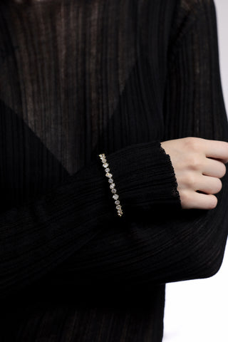 CLOSE UP OF A MODEL’S WRIST WITH HER ARMS FOLDED IN FRONT OF HER, AS SHE WEARS A SHEER BLACK DRESS AND THE CELINE MULTI CZ HINGE BRACELET