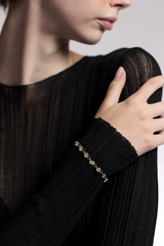 CLOSE UP OF A MODEL’S WRIST RESTING AGAINST HER SHOULDER, AS SHE WEARS A SHEER BLACK DRESS AND THE CELINE MULTI CZ LINE BRACELET