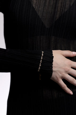 CLOSE UP OF A MODEL’S WRIST WITH HER HAND RESTING AGAINST HER TOSRO, AS SHE WEARS A SHEER BLACK DRESS AND THE CELINE ADJUSTABLE BOLO BRACELET