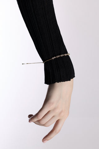 A WRIST AND HAND OUTSTRETCHED AGAINST A WHITE BACKGROUND, WITH THE CELINE ADJUSTABLE BOLO BRACELET LAYERED OVER A LONG BLACK SLEEVE
