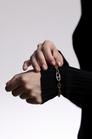CLOSE-UP OF A HAND OUTSTRETCHED WEARING A SHEER BLACK SLEEVE AND THE CELINE ANCHOR LINK BRACELET, AS THE OPPOSITE HAND PLAYS WITH THE BRACELET LINKS