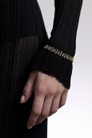 CLOSE UP OF A HAND AT A MODEL’S SIDE, AS SHE WEARS A SHEER BLACK DRESS AND THE CELINE GEO LINE BRACELET LAYERED OVER THE SLEEVE