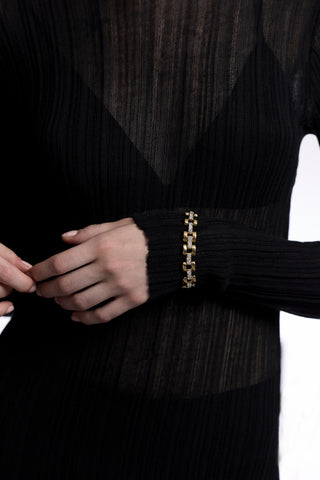 A CLOSE UP OF A MODEL’S TORSO WITH HER HAND ACROSS HER STOMACH, AS SHE WEARS A SHEER BLACK DRESS AND THE CELINE WATCH CHAIN BRACELET