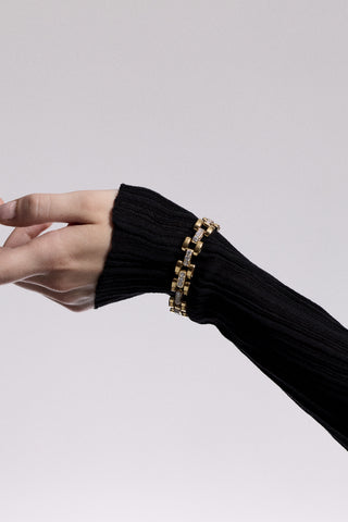 AN ARM AND WRIST OUTSTRETCHED, WEARING A SHEER BLACK SLEEVE AND THE CELINE WATCH CHAIN BRACELET LAYERED OVER IT