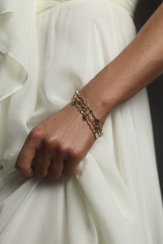 CLOSE UP OF A MODEL’S ARM HOLDING HER WHITE DRESS AND WEARING THE HERA MULTI 3 LAYER LINE BRACELET