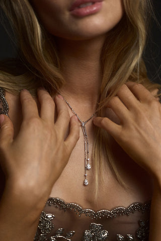 CLOSE UP OF A MODEL’S CHEST WITH HER HANDS LIFTED UP TO HER SHOULDERS, WEARING A BLACK DRESS AND THE HERA FAUX LARIAT NECKLACE