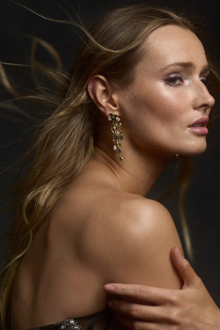 SIDE PROFILE OF A MODEL WITH HER BLONDE HAIR FLOWING BEHIND HER, AS SHE WEARS A STRAPLESS DRESS AND THE HERA MULTI CHANDELIER EARRINGS